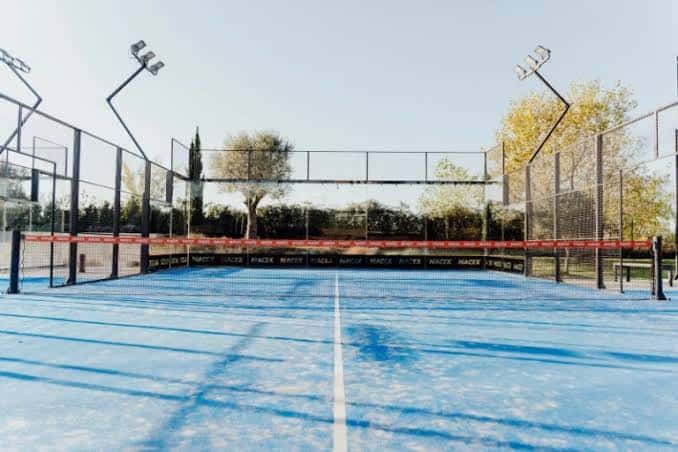 Vista frontal de una pista de pádel azul con red y luces en un día soleado