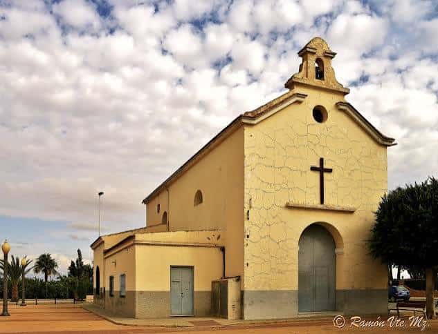 Fachada lateral de la Iglesia de Balsares con cruz y cielo nublado
