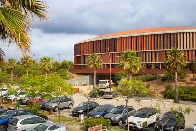 Fachada moderna del pabellón polideportivo rodeado de palmeras y aparcamiento