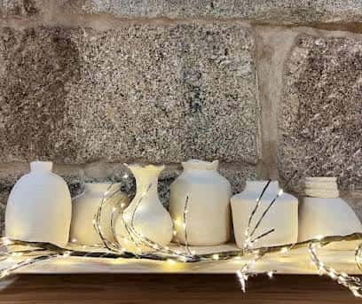 Piezas de cerámica cruda decoradas con luces cálidas sobre una repisa de piedra