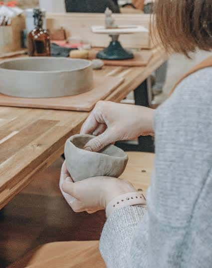 Detalle de manos modelando un recipiente de arcilla en la mesa de trabajo