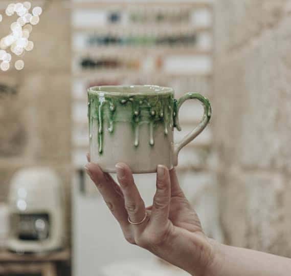 Taza de cerámica esmaltada en verde sostenida por una mano en primer plano