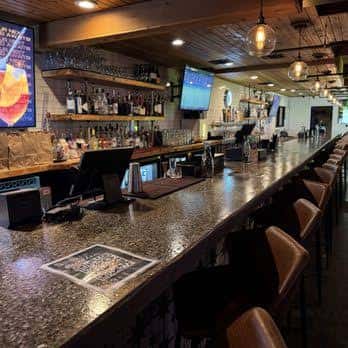 Interior del bar con mostrador largo, taburetes de cuero y estanterías de botellas