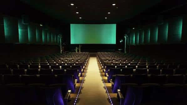 Sala de cine vacía con butacas azules y pantalla verde iluminada