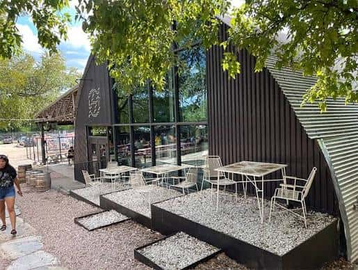 Área de patio exterior con mesas blancas y vegetación alrededor del edificio