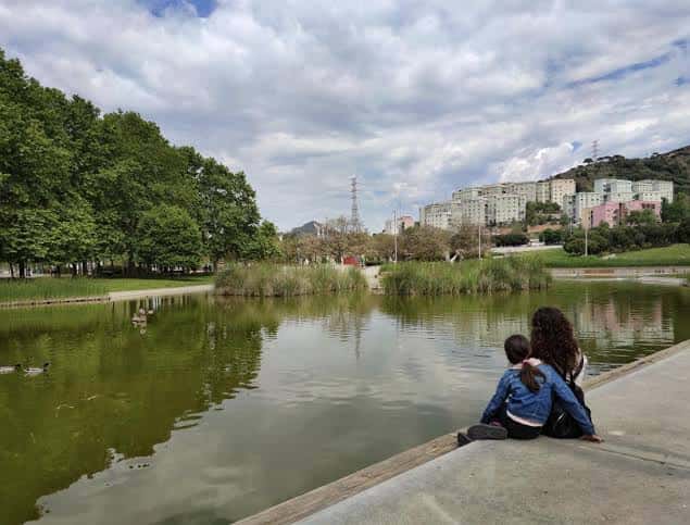 Lago del parque con personas relajándose junto al agua y edificios urbanos al fondo