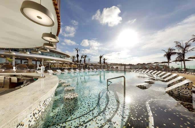 Vista panorámica de la piscina principal del Hard Rock Hotel Tenerife con tumbonas y palmeras bajo el sol