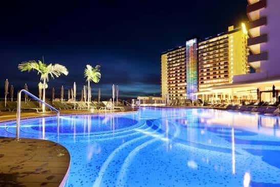 Piscina iluminada por la noche frente al edificio del hotel con luces LED en la fachada
