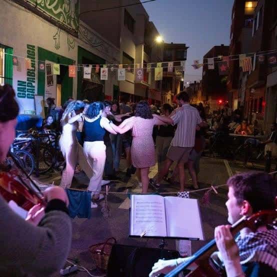 Celebración callejera con gente bailando al son de violines