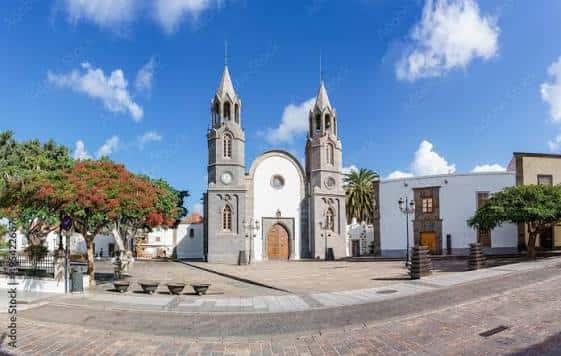 Vista panorámica de la plaza frente a la Basílica de San Juan Bautista en Telde, con árboles y edificios coloniales