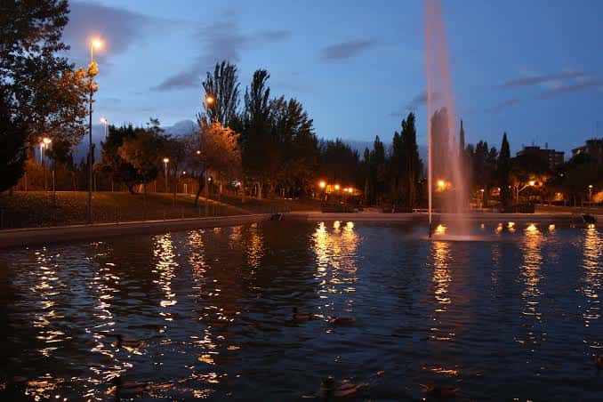 Vista nocturna del parque con fuente iluminada y reflejos en el agua