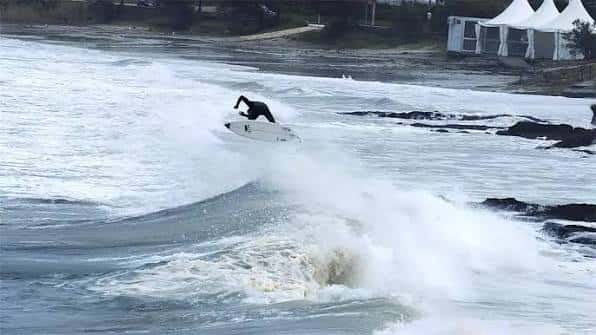 Surfista realizando un giro sobre una ola con tiendas blancas al fondo