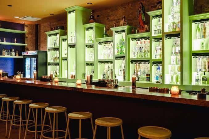 Interior del bar Las Perlas con estanterías verdes iluminadas y barra de madera