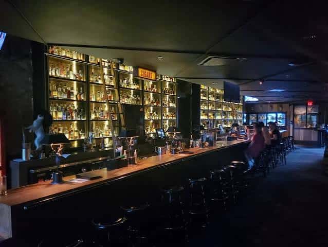Barra larga con múltiples botellas en estantes traseros y ambiente nocturno