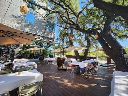 Terraza al aire libre con mesas para eventos bajo árboles y sombrillas
