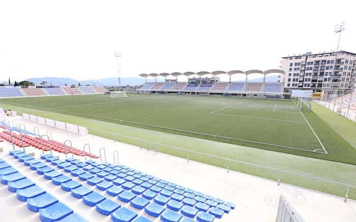 Interior del estadio mostrando asientos azules y rojos, césped verde y estructura moderna