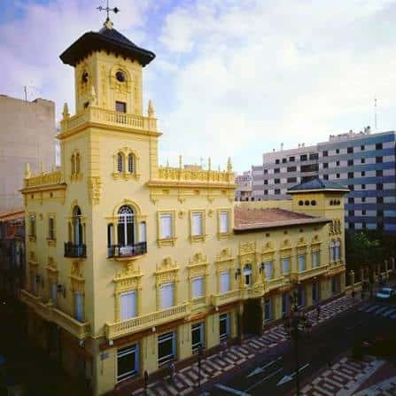Vista aérea del edificio amarillo con tejado oscuro y entorno urbano