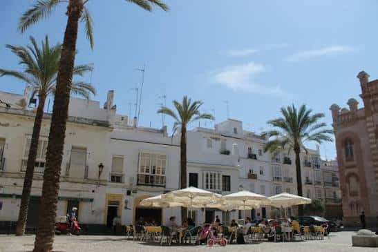 Plaza Fragela con terrazas de cafetería bajo sombrillas y edificios blancos al fondo
