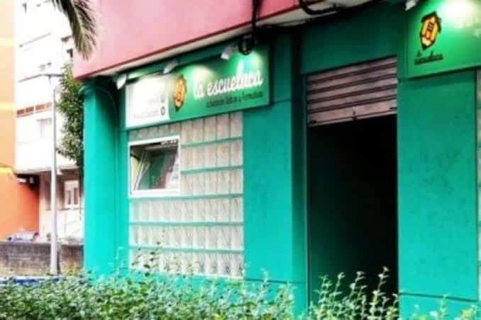 Fachada exterior de La Escueluca con su distintiva pared verde y letrero iluminado