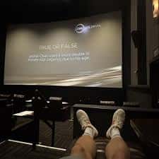 Interior de sala de cine con butacas reclinables y pantalla mostrando contenido interactivo