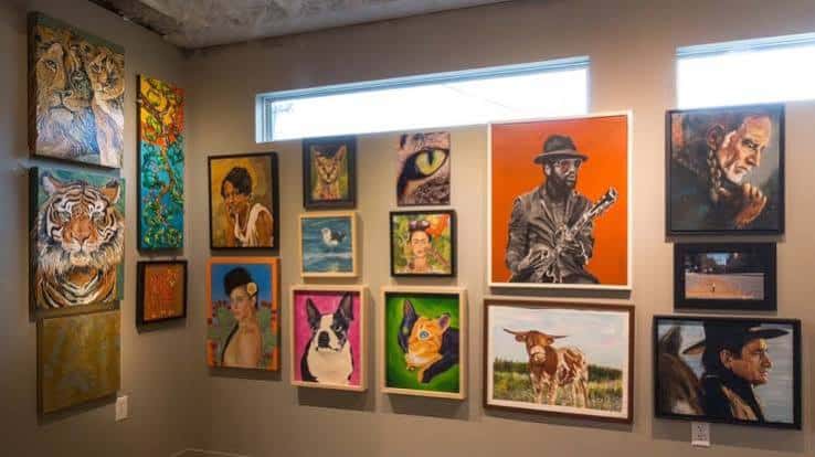 Interior de la galería mostrando una pared con diversas obras de arte enmarcadas