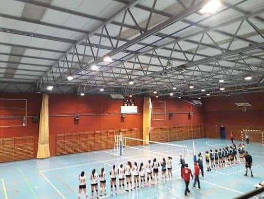 Interior del pabellón deportivo con cancha de voleibol y equipos alineados