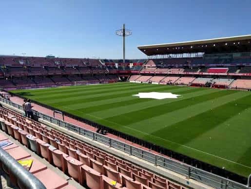 Vista interior del estadio con gradas rojas y campo de césped bajo cielo despejado