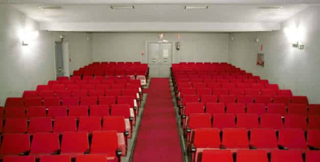 Sala de espectáculos con filas de asientos rojos y pasillo central