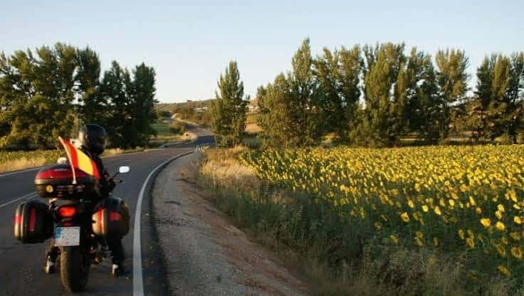 Moto con bandera española en carretera rural junto a campo de girasoles