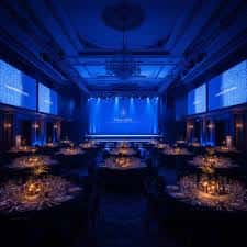 Sala de eventos decorada con mesas redondas y luces azules para una cena o gala