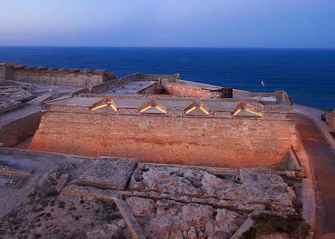 Panorámica nocturna del Fuerte de Victoria Grande iluminado junto al mar Mediterráneo
