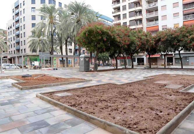 Plaza en proceso de reurbanización con zonas de tierra preparadas para jardinería
