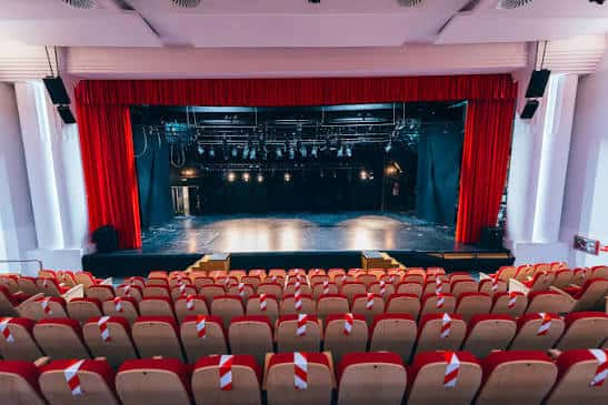 Vista del auditorio vacío con butacas rojas y cortinas de escenario