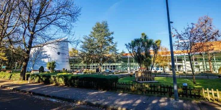 Paisaje del parque con edificios de cristal, árboles y caminos peatonales bajo cielo despejado
