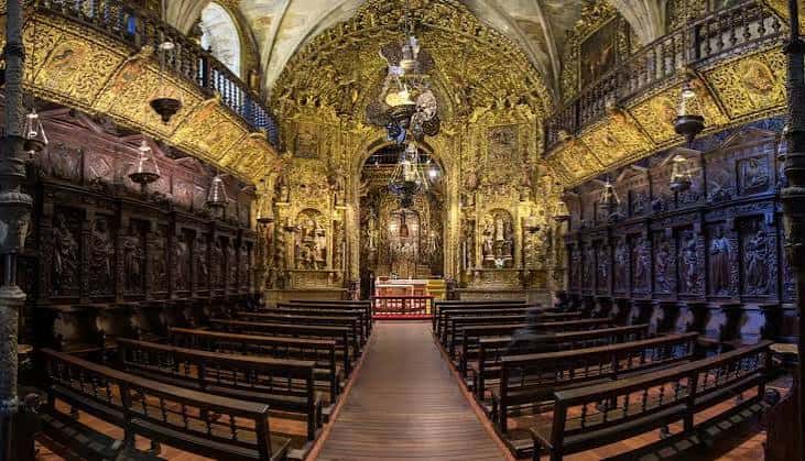 Vista interior de la iglesia con retablo dorado y bancos de madera