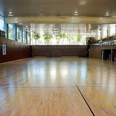 Vista general del pabellón deportivo con suelo de madera y canastas