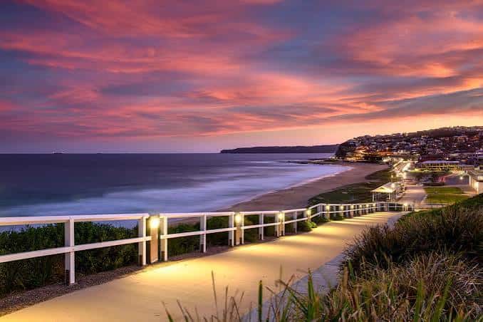 Paseo costero iluminado al atardecer con cielo colorido sobre Dixon Park Beach