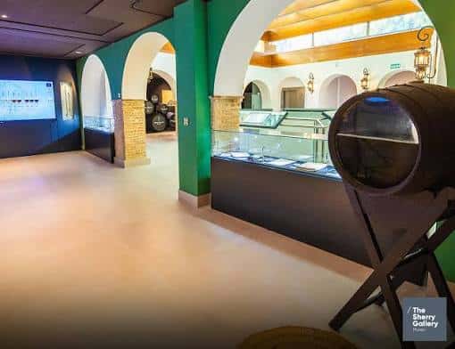 Interior de The Sherry Gallery con arcos verdes y exposición de barricas de vino