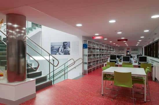 Interior moderno de la biblioteca con estanterías, mesas y sillas verdes