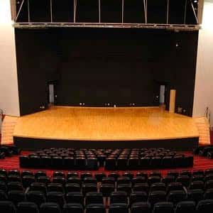 Interior del auditorio vacío con escenario de madera y butacas rojas