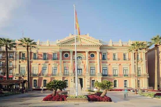 Vista frontal de la Casa Consistorial de Murcia con fachada neoclásica y bandera española