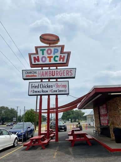 Letrero icónico de Top Notch Hamburgers con mesas rojas en el área de servicio para llevar