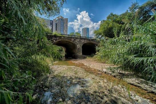 Puente histórico de piedra sobre el arroyo rodeado de vegetación densa