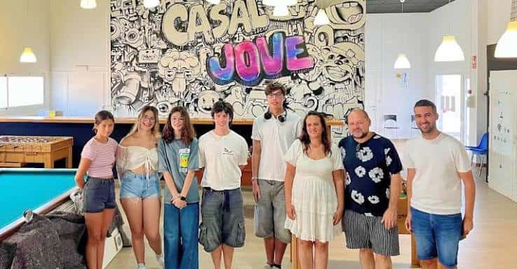 Grupo de jóvenes y adultos posando frente al mural interior del Casal Jove