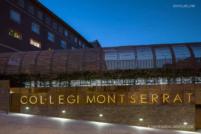 Fachada iluminada con el nombre 'COL·LEGI MONTSERRAT' en letras doradas al atardecer