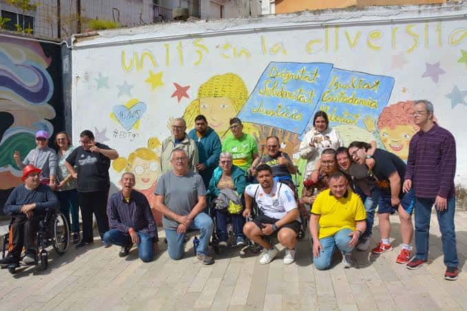 Grupo diverso de personas reunidas frente a un mural comunitario en el exterior del centro