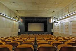 Interior del auditorio con butacas naranjas y pantalla de cine