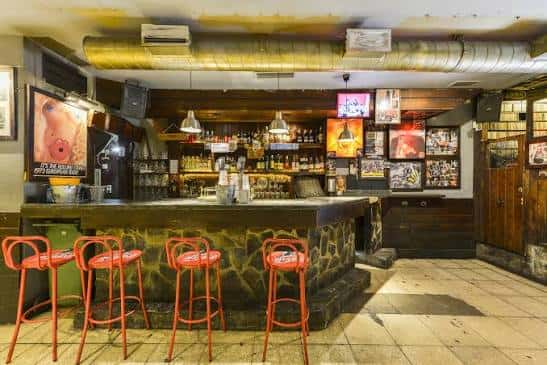 Vista del mostrador del bar con taburetes rojos y estanterías de bebidas