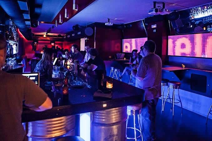Interior del bar con iluminación de neón y clientes en la barra