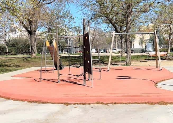 Área recreativa infantil con columpios y superficie de goma roja